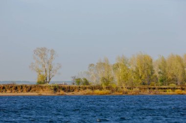 Sonbahar manzarası, koyu mavi su, son sıcak günler, nehir, ağaçlar, rüzgarlı hava, sarı-kırmızı sonbahar yaprakları.