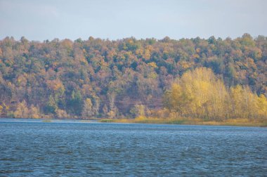 Sonbahar manzarası, koyu mavi su, son sıcak günler, nehir, ağaçlar, rüzgarlı hava, sarı-kırmızı sonbahar yaprakları.