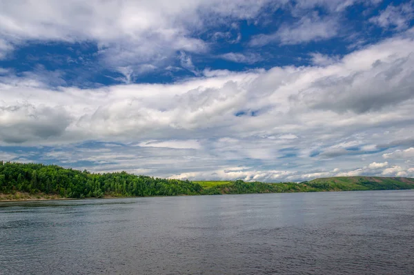Yaz fotoğrafı, güçlü gök gürültülü bulutlar, mavi gökyüzü, karanlık keskin su, Kama Nehri boyunca turist yürüyüşü.