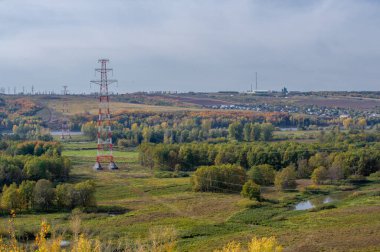 Avrupa 'nın kırsal kesimlerinde, bir sonbahar günü, yerel Avrupa ağaçlarının ve bitki örtüsünün üzerinde yükselen yüksek voltajlı elektrik iletim kulelerinin panoramik görüntüsü