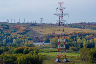Avrupa 'nın kırsal kesimlerinde, bir sonbahar günü, yerel Avrupa ağaçlarının ve bitki örtüsünün üzerinde yükselen yüksek voltajlı elektrik iletim kulelerinin panoramik görüntüsü