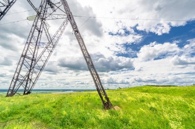 Yaz manzarası, nehir kenarındaki yüksek voltajlı kutuplar, bulutlardaki kasvetli gökyüzü, elektrik erozyonu.
