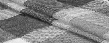 Doku, arkaplan, ipek atkı siyah beyaz, metal şeritli. Eşarp, soyut İskoç motifleriyle pastel renklerle hassas bir yama deseniyle süslenmiş. kontrol edilen kumaş