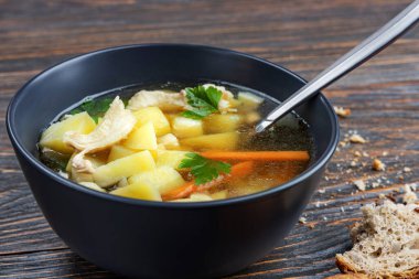 Tavuklu şehriye çorbası ve tahta tabakta otlar, sığ alan derinliği, seçici odaklanma. Sağlıklı ev beslenmesi kavramı.