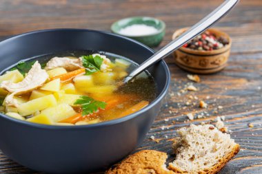 Tavuklu şehriye çorbası ve tahta tabakta otlar, sığ alan derinliği, seçici odaklanma. Sağlıklı ev beslenmesi kavramı.