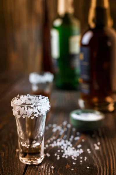 An empty tequila glass, with salt at the edges, stands on the bar, in the background are different bottles of alcohol, shallow depth of field, selective focus. The concept of a drink in the bar. — Stock Photo, Image
