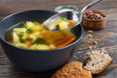 Tavuklu şehriye çorbası ve tahta tabakta otlar, sığ alan derinliği, seçici odaklanma. Sağlıklı ev beslenmesi kavramı.