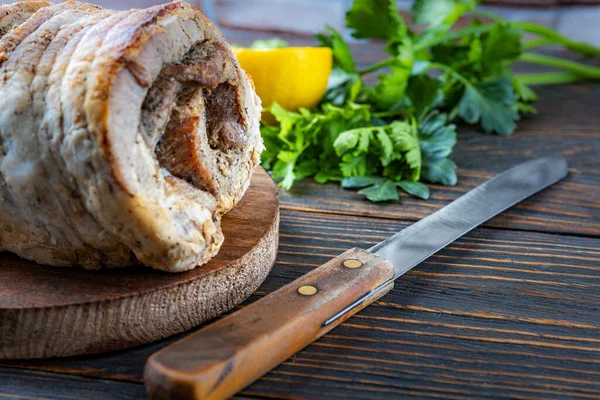 Leckeres gebratenes Schweinefleisch in Kräutern und Gewürzen in Nahaufnahme des ganzen Körpers auf einem Holzbrett gebacken, daneben ein Messer, Zitrone, Kräuter und Gewürze, geringe Schärfentiefe, selektiver Fokus. — Stockfoto