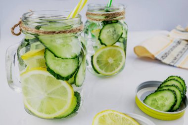 Soğuk içecek, beyaz arka planda salatalık ve limonlu iki retro cam kavanoz, sığ alan derinliği, seçici odaklanma. Sağlık içeceği kavramı.