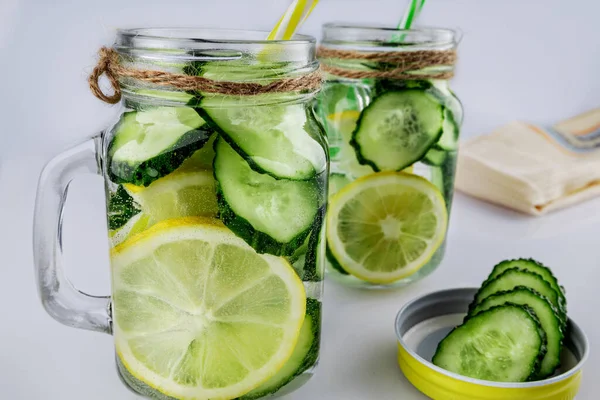 Κρύα ποτά, δύο ρετρό γυάλινα βάζα λεμονάδας με αγγούρι και λεμόνι σε λευκό φόντο, ρηχό βάθος πεδίου, επιλεκτική εστίαση. Έννοια ροφήματος υγείας. — Φωτογραφία Αρχείου