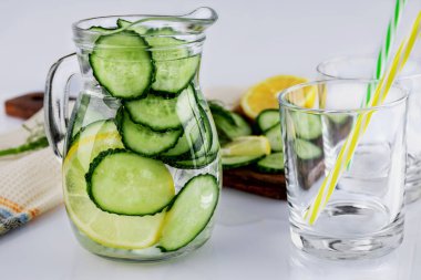 Salatalık ve limondan yapılmış soğuk bir içecek sürahide ev yapımı limonata ve beyaz arka planda seçici bir odak noktası olan iki boş bardak. Sağlıklı içki konsepti