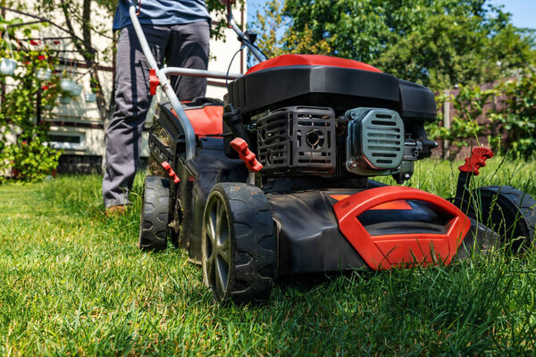 A man moves with a lawn mower and mows green grass. Garden care concept