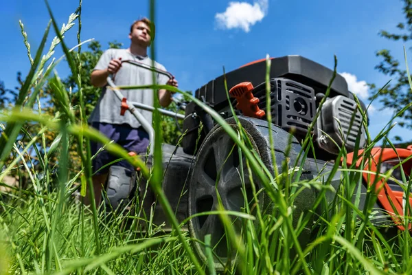 Een man beweegt met een grasmaaier en maait groen gras. Tuinonderhoud concept — Stockfoto
