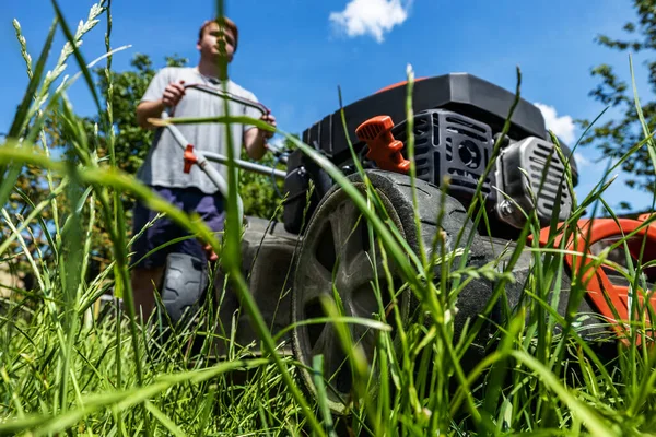 Een man beweegt met een grasmaaier en maait groen gras. Tuinonderhoud concept — Stockfoto