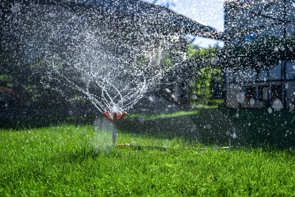 Nowoczesne urządzenie ogrodu nawadniającego. System nawadniania - technika podlewania w ogrodzie. Zraszacz trawnika opryskujący wodą zieloną trawę. — Zdjęcie stockowe