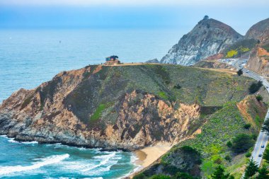 Pasifik, Kaliforniya yakınlarındaki Gray Whale Cove Trail yakınlarındaki 1. Otoyol kıyı şeridi, okyanus dalgaları, engebeli uçurumlar ve Pasifik kıyısı boyunca yemyeşil tepeler.