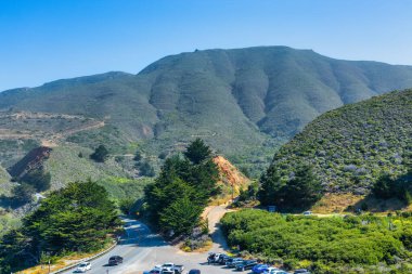 Pasifik, Kaliforniya yakınlarındaki Gray Whale Cove Trail yakınlarındaki 1. Otoyol kıyı şeridi, okyanus dalgaları, engebeli uçurumlar ve Pasifik kıyısı boyunca yemyeşil tepeler.