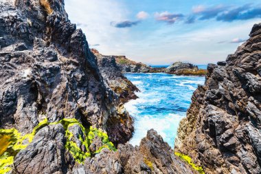 Dramatic Big Sur coastline along Highway 1, California. Waves crash against rugged cliffs, forming turquoise patterns in the Pacific Ocean, showcasing the raw beauty of the California coast