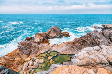 Dramatic Big Sur coastline along Highway 1, California. Waves crash against rugged cliffs, forming turquoise patterns in the Pacific Ocean, showcasing the raw beauty of the California coast