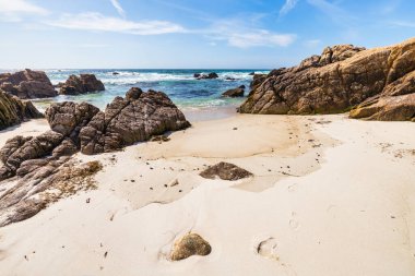 Secluded sandy beach along 17 Mile Drive in Monterey, California. Golden sand, rocky cliffs, and turquoise Pacific waters create a peaceful coastal escape on this famous scenic route