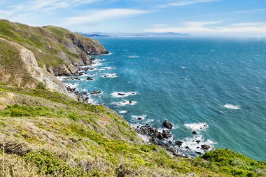 Scenic view from Tennessee Valley Trail in Marin Headlands, California. Rolling green and golden hills open toward the Pacific Ocean with distant views of San Francisco and the Bay Area skyline