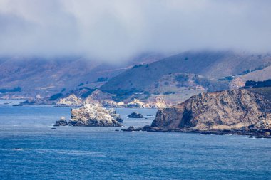 Rocky Big Sur coastline near Point Sur Lighthouse, California, USA. Scenic view of rugged cliffs, Pacific Ocean waves, and coastal fog drifting over the mountains along Highway 1