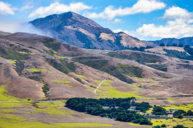 Scenic mountains and rolling hills of Big Sur near Point Sur Naval Facility, California. Dry rugged slopes with green patches under bright sky along Pacific Coast Highway 1