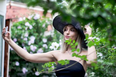 Şapkalı bir akıllı telefon kullanan genç şık güzel kadın selfie açık havada yapma