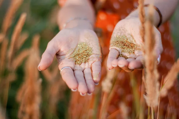 Posing female hands in golden glitter in the field background