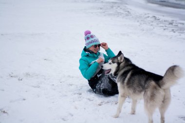 Genç kadın sahilde denize yakın Karda husky ile eğlenmek. Kar hava.