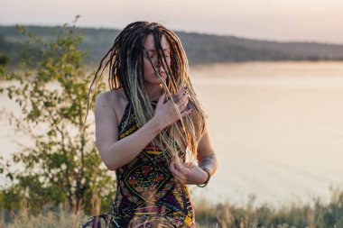 Genç güzel hippi kadın vahşi dans alanında günbatımında dreadlocks ile