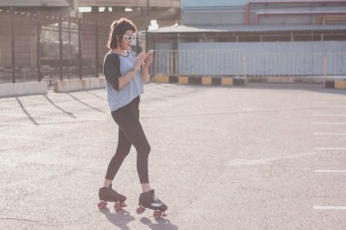 Dans ve having fun şık güzel genç kadın gözlük ve denim ceket paten. Gülümseyen ve gün batımında poz. Kent, Belediye, silindirler