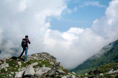 Sırtında büyük bir sırt çantası ile turist dağın zirvesinde duruyor, bir eylem kamera elinde tutuyor ve fotoğraf çeker