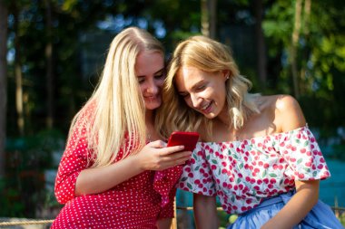 iki arkadaş parkta iyi eğlenceler, bir akıllı telefon kullanıyorlar