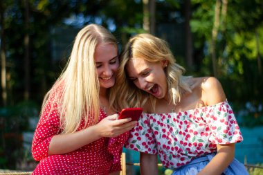 iki arkadaş parkta iyi eğlenceler, bir akıllı telefon kullanıyorlar