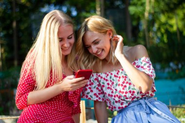 iki arkadaş parkta iyi eğlenceler, bir akıllı telefon kullanıyorlar