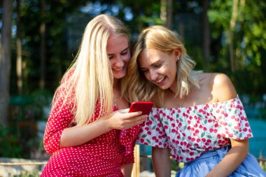 iki arkadaş parkta iyi eğlenceler, bir akıllı telefon kullanıyorlar