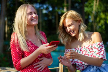 iki arkadaş parkta iyi eğlenceler, bir akıllı telefon kullanıyorlar