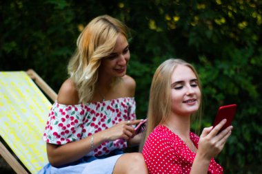 iki arkadaş parkta iyi eğlenceler, bir akıllı telefon kullanıyorlar
