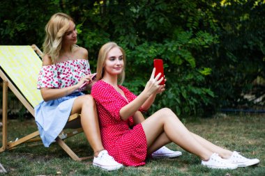 iki arkadaş parkta iyi eğlenceler, bir akıllı telefon kullanıyorlar