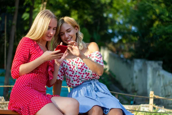 iki arkadaş parkta iyi eğlenceler, bir akıllı telefon kullanıyorlar
