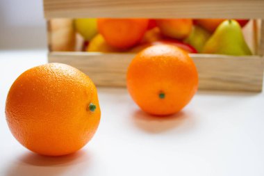 Beyaz zemin üzerinde bir kutu içinde portakal, armut, mango ve limon vardır.