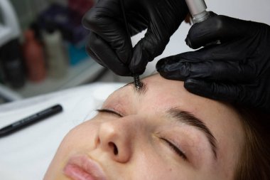 Microblading kaşlar iş akışında bir güzellik salonu. Renkli ona göz kaşları olan kadın. Kaşları için yarı kalıcı makyaj. Modelin yüzü ve kaş odaklanmak