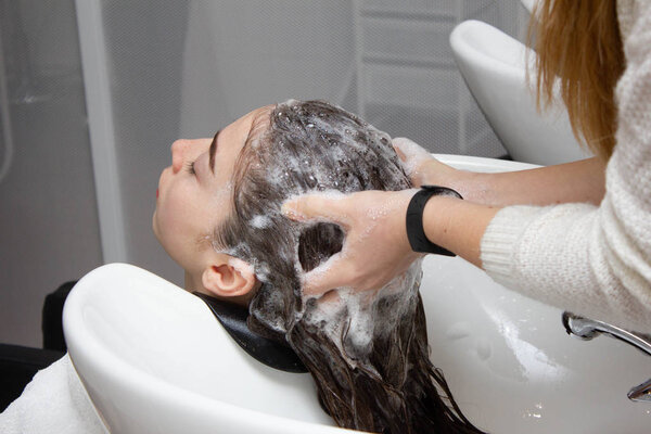 Woman applying shampoo and massaging hair of a customer. Woman having her hair washed in a hairdressing salon.
