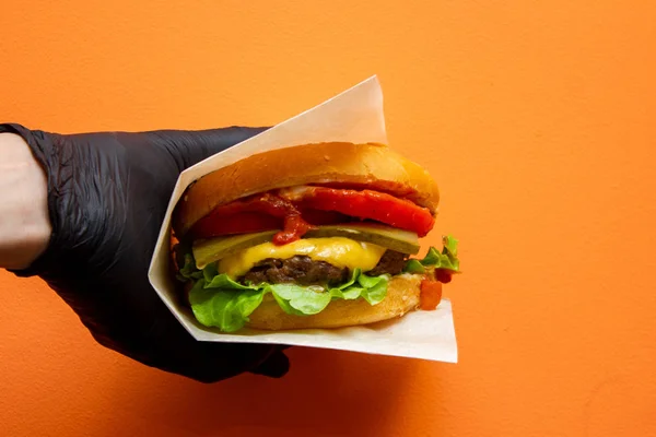 fresh tasty burger in the hand on orange background