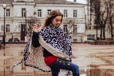 Yağmurluk ve lastik çizmeli şık kadın su birikintilerinde yürür ve eğlenir