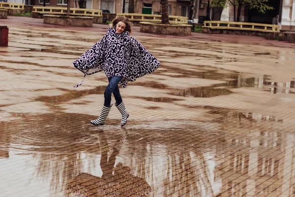 レインコートとゴムブーツのスタイリッシュな女性は 水たまりを歩いて楽しんでいます — ストック写真