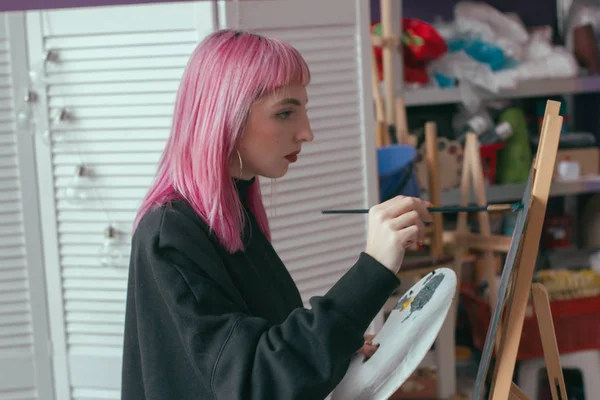 ピンクの髪を持つゴージャスな女性アーティストは アートスタジオで彼女の手にパレットでアートプロジェクトに取り組んでいます 若い女性が絵を描く — ストック写真