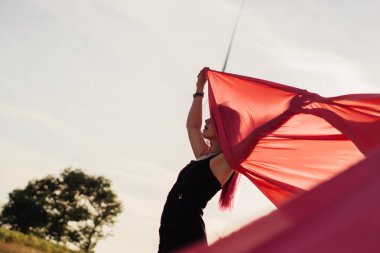 Pembe saçlı genç kadın pembe kumaş parçaları ile rüzgar jeneratörleri ile alan yakınında dans . Gün batımında yel değirmeni. Moda portresi