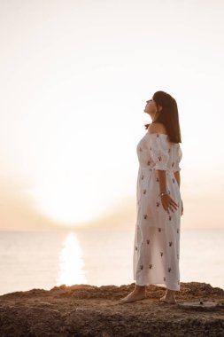 güzel genç brunete kadın sahilde güzel bir görünüm sahiptir ve iyi bir gündoğumu zamanı vardır. Rahatla